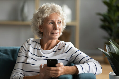 woman smiling while sitting on couch and using cell phone