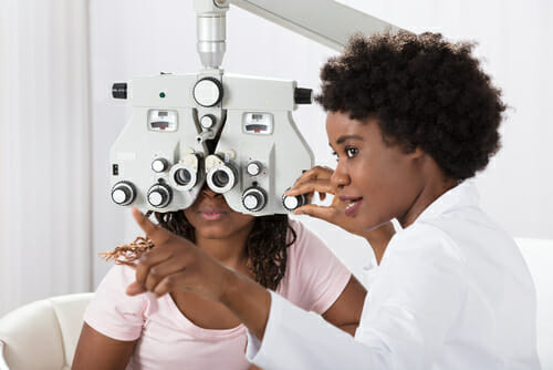 A doctor pointing in front of a patient who is looking through an instrument of ophthalmology 